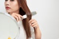 Getting rid of tangles. Beautiful young woman looking at her reflection in mirrorand brushing her long hair while sitting at the