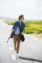 Getting some musical inspiration on the open road. Trendy young male wearing sunglasses walking down the middle of a Royalty Free Stock Photo