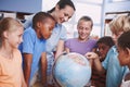 Getting to know their geography. A group of children looking at a world globe during geography class.