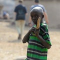 Unidentified Ghanaian boy in striped shirt holds a wooden objec