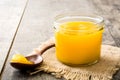 Ghee or clarified butter in jar and wooden spoon on wooden table.