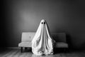 Ghost covered with a white ghost sheet on a sofa in the living room. Halloween concept