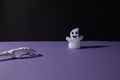 Ghost decoration for Helloween and hand bones on purple black background with copy space. Minimal flat lay concept