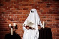 Ghost holding book and wine over brick background. Halloween party. Royalty Free Stock Photo