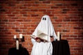 Ghost holding book and wine over brick background. Halloween party. Royalty Free Stock Photo