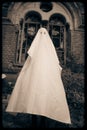 A ghost stands against the backdrop of an old crypt on a graveyard. The vintage image evokes themes of the paranormal and the Royalty Free Stock Photo
