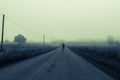 A ghostly blurred man standing in the middle of the road on an eerie misty morning. With a dark, moody colour edit