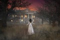 Ghostly figure of woman in long white dress floating through forest towards a creepy haunted mansion house. 3d rendering Royalty Free Stock Photo