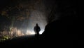 A ghostly transparent hooded figure silhouetted against a glowing bright light on a country road. On a foggy winters night