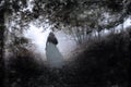 A ghostly woman in a white dress. Walking along a path in a forest path. On a moody foggy autumn day. With a grunge, vintage edit Royalty Free Stock Photo