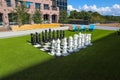 A giant black and white chess set on lush green grass surrounded by lush green and autumn colored trees near buildings Royalty Free Stock Photo