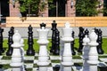 A giant black and white chess set on lush green grass surrounded by lush green and autumn colored trees near buildings Royalty Free Stock Photo