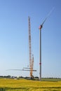 Giant construction site for a wind turbine, crane is lifting the second blade to install it onto the tower, heavy industry for Royalty Free Stock Photo