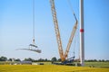 Giant crane lifting a wind turbine blade to install it onto the tower, heavy industry construction site, concept for electricity,