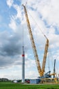 Giant crane is moving a tower part from steel of a wind turbine onto the first tube, heavy industry construction site for a power