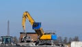 A giant excavator at work outside an industrial steel and cement area