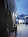 Giant icicles on a residential house on a gray wall, winter in the snow, in the evening with backlight