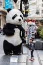 A giant Panda figure outside shops and Restaurants in main city pedestrian street, with exciting little girl