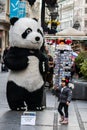 A giant Panda figure outside shops and Restaurants in main city pedestrian street, with exciting little girl