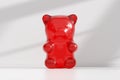 Giant red gummy bear sitting in a house interior with white wall and floor