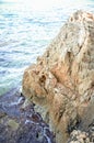 Giant rock textured cliff corner isolated in the blue sea calm waters on sunny day light Royalty Free Stock Photo