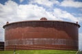 Giant rusty oil tank in tank farm in Cushing Oklahoma behind barbed wire fence with pretty blue sky background