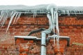 large melting icicles hanging from the iron drainpipe of an old brick building, viewed from below Royalty Free Stock Photo