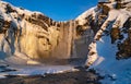 Giant Skogafoss waterfall completely covered with snow and the river passes next to it. The dawn sun illuminates the water that