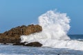 Giant wave breaking against large rock. Spray in the air; blue sky in the distance.