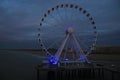 Giant wheel placed on a pier above the ocean in the night with a blue glare over it