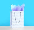 Gift bag with paper on white table against light blue background Royalty Free Stock Photo