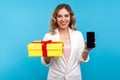 Gift, bonuses in mobile tariff. Portrait of cheerful woman showing wrapped present box and cell phone. blue background Royalty Free Stock Photo