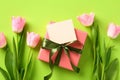 Gift box with blank greeting card mockup, pink tulips flowers on green table. Happy Mothers Day flat lay composition. Top view Royalty Free Stock Photo