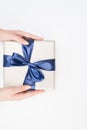 Gift-box with blue ribbon. Woman`s hands are holding present box with dark blue bow on a isolated background. Bakground for your Royalty Free Stock Photo