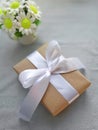 Gift box with bowknot, bouquet of daisies on grey fabric background.