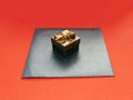 Gift box in bronze color with a bow and a black craft envelope on a red background Royalty Free Stock Photo