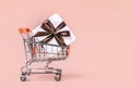 Gift box with brown bow in miniature shopping cart on pastel coral background with copy space