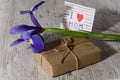 Gift box, card from child with message for mom, iris flower on gray wood table in morning sunlight. Happy Mother`s Day