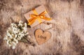 A gift box with a gold bow, white flowers and a wooden heart. A small present with a gold ribbon on a wooden background. Royalty Free Stock Photo