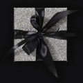 Silver glittering gift box package with black ribbon bow isolated on black background, top view, black friday concept Royalty Free Stock Photo