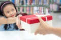 Gift box for kids girl. White box with red bow in the smiling asian girl hands for give a gift in the library.