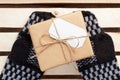 Gift box packed brown paper and twine with blank white address card on handmade mittens lying on wooden grid panel top view