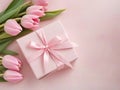 Gift box with pink tulips on table on pink backgound with copy space