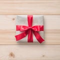 Gift box present isolated with clipping path with red bow satin ribbon over brown wrapping paper on white pine wood background Royalty Free Stock Photo