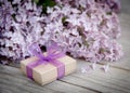 Gift box with purple bow and lilac on wood