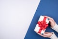 Gift box with a red bow on a gray and blue background in women`s hands. Space for text. Royalty Free Stock Photo