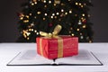 Gift. Box in red packaging. Golden bow. A gift on a book of the Bible. On the background of the Christmas tree