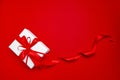 Gift box with red ribbon bow on red background, top view. White holiday gift box, present Royalty Free Stock Photo