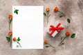 Gift box with red ribbon and small roses on beige background, blank paper card mockup. Greeting and invitation card template. Top Royalty Free Stock Photo