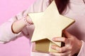 Gift box in the shape of a gold star in the hands of a young Asian girl. on a pink isolated background